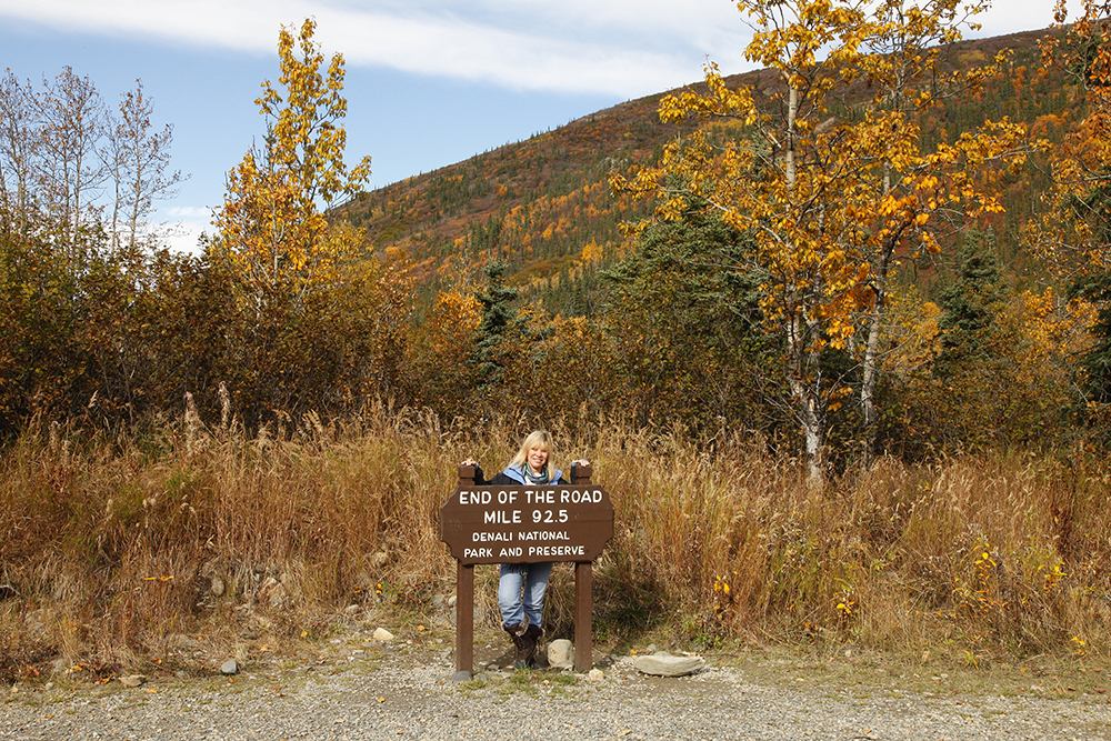 a woman standing near a board that says End of the road mile